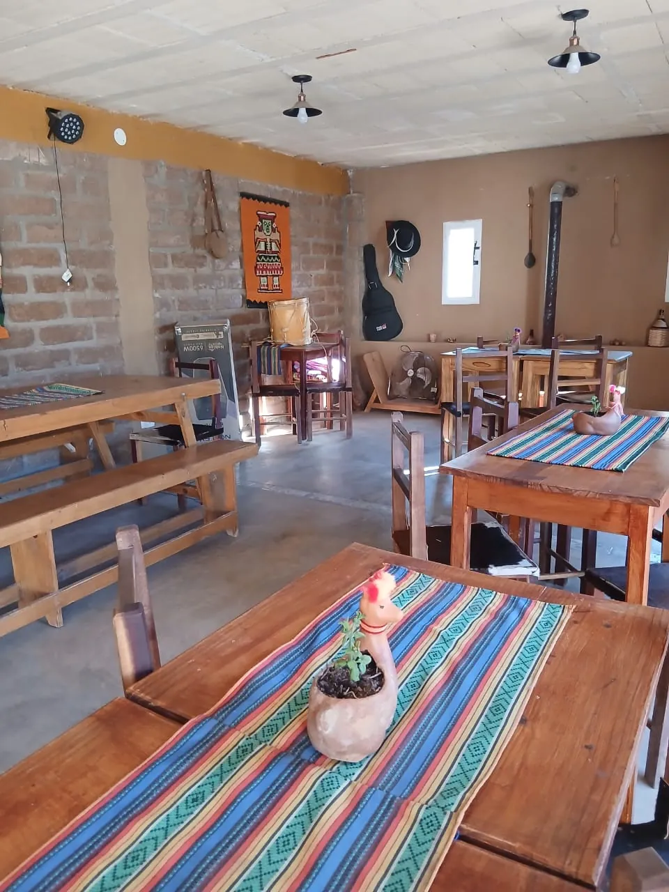 Quincho con mesas largas de madera, caminos de telar y paredes de adobe